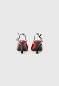 Zapatos de tacón slingback de charol rojo con tacón de aguja negro. Con tira de logo en blanco y negro en la parte posterior. Textura suave.