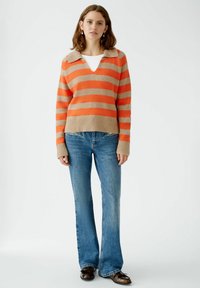 Gestreifter Pullover in Orange und Beige mit V-Ausschnitt und Kragen, kombiniert mit weit geschnittenen blauen Jeans und braunen Schuhen. Gerippter Saum und Bündchen.