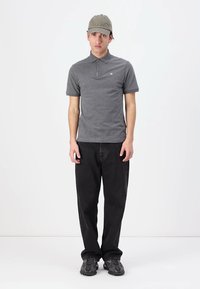 Šedé polo tričko s krátkými rukávy, černé džíny a šedá kšiltovka. Model stojí vzpřímeně, boty mají texturovaný design.