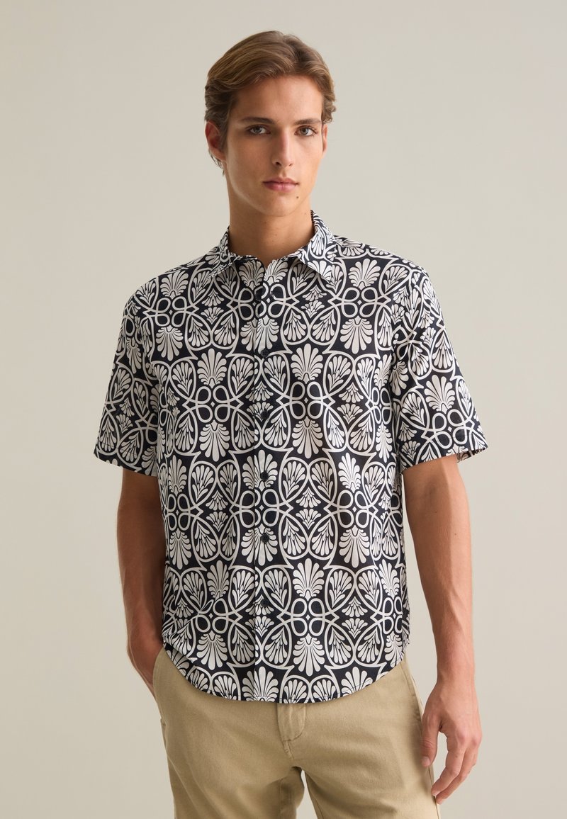 Korte mouw shirt met een zwarte achtergrond en wit bloemmotief. Heeft een klassieke kraag en knoopsluiting met een ontspannen pasvorm.
