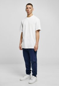 Camiseta de algodón blanca, corte relajado, combinada con joggers azul marino. Calzado: zapatillas blancas. Diseño liso; sin logos ni patrones visibles.