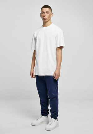 White cotton t-shirt, relaxed fit, paired with navy joggers. Footwear: white sneakers. Plain design; no visible logos or patterns.