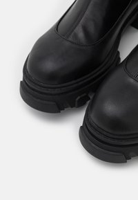 Black leather ankle boots with a rounded toe, thick treaded sole, and textured accents. Smooth finish with contrasting stitching details.