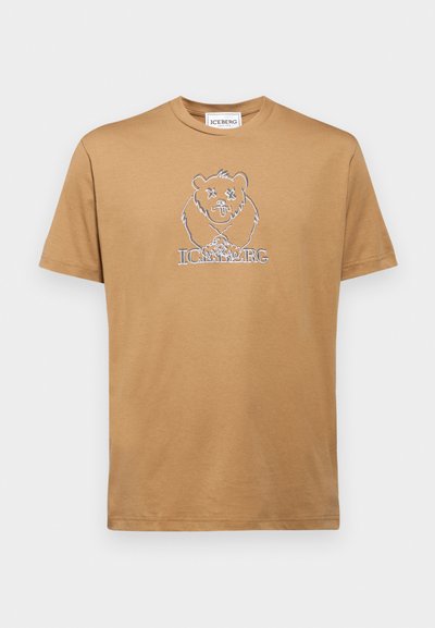T-shirt en coton beige avec un graphique d'un ours aux yeux croisés et le mot "ICEBERG" en blanc en dessous du design. Manches courtes, col rond.