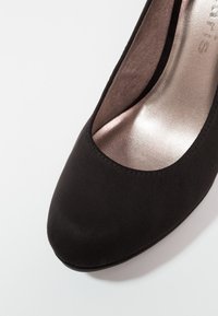 Chaussure à talon haut en suède noir avec un bout arrondi et un intérieur lisse et métallique. Présente un design simple sans embellissements.