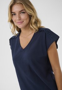 Top de color azul marino con escote en V y mangas cortas y holgadas. Acento de encaje en los hombros, textura suave, ajuste casual, diseñado para la comodidad.