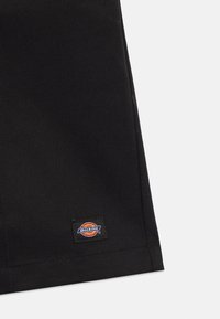 Černá bavlněná tkanina s diagonální vazbou. Obsahuje obdélníkovou etiketu s vícebarevným kruhovým logem s nápisem "Dickies."