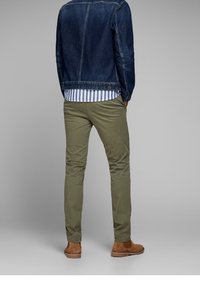 Veste en denim bleu foncé, chemise rayée en dessous, chinos verts et chaussures en daim marron. Textures lisses et style décontracté sont mis en avant.