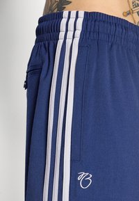 Atletske kratke hlače mornarsko plave boje izrađene od meke tkanine, s bijelim bočnim prugama, elastičnim pojasom, stražnjim džepom i detaljem s logotipom.