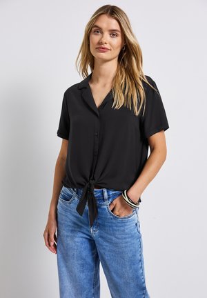 Sort kortærmet bluse med krave og frontknude-detalje, parret med lyseblå denim jeans. Glat tekstur, afslappet pasform.