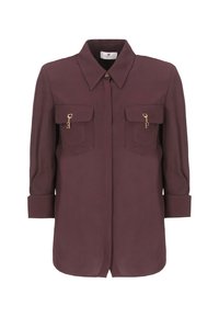 Blusa bordeaux con colletto, due tasche sul petto e dettagli in metallo dorato. Maniche lunghe ribaltate fino ai gomiti, tessuto morbido con una texture liscia.