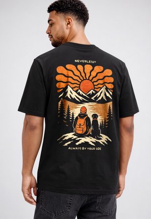 Man wearing black t-shirt with graphic of person and dog sitting on hill, mountains, trees, sunset, and text "Neverless" and "Always by your side."