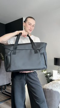 Juoda minkšto audinio rankinė su dviem rankenomis ir užtrauktuko uždarymu. Turi priekines ir šonines kišenes, pagaminta iš tvirto audinio, minimalistinio dizaino.