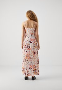 Maxi sukienka na cienkich ramiączkach, wzór kwiatowy w odcieniach brzoskwiniowym, różowym i fioletowym, lekki materiał oraz luźny krój. Czarne buty dopełniają stylizację.