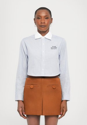 Cropped, blue and white checkered shirt with a white collar; front buttons; embroidered logo. Paired with a brown suede mini skirt with pockets.