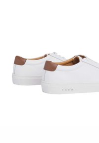 Baskets en cuir blanc avec des accents marron à l'arrière, forme arrondie, surface texturée et semelle en caoutchouc blanche. Nom de la marque visible.