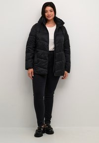 Giacca a vento nera con cappuccio, caratterizzata da un design trapuntato e cordino regolabile. Abbinata a jeans skinny neri e scarpe nere.