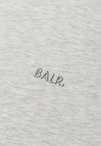 Světle šedá textilie s jemnou texturou a vyšívaným slovem "BALR." v tmavě šedé niti, umístěným výrazně na látce.