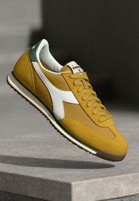 Kollane tekstiilne jalats valgete aktsentidega, rohelise kandaga ja tekstuursete võrkpaneelidega; kummist tallaga, millel on pruun mustripinna mustris haarduvus.