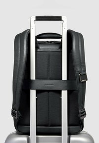 Zwarte rugzak van gestructureerd materiaal, met gevoerde riemen en een bovenste handvat, bevestigd aan een uitschuifbare zilveren trolleyhandgreep.