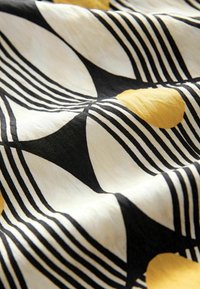 Tissu en coton présentant un motif géométrique en blanc, noir et or, avec des formes courbes et des lignes alternées créant une texture visuelle.