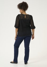 Zwarte blouse met een hexagonaal patroon, doorzichtige stof, puffmouwen en een sleutelgatdetail aan de achterkant, gecombineerd met donkerblauwe slim-fit jeans.