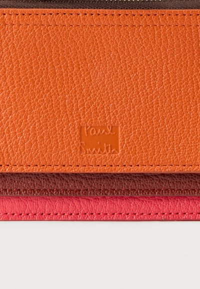 Στοίβα από τρία πορτοφόλια από υφή δέρματος σε πορτοκαλί, σκούρο καφέ και κόκκινο, με ανάγλυφο λογότυπο Paul Smith στο πορτοκαλί πορτοφόλι.