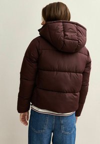 Giacca a vento marrone scuro con cappuccio, design a quadri e polsini elasticizzati. Abbinala a un top bianco stratificato e a jeans in denim blu.