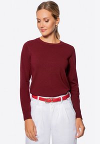 Maglione a maglia bordeaux con maniche lunghe, scollo rotondo, abbinato a pantaloni bianchi e una cintura rossa. Texture liscia, design aderente.