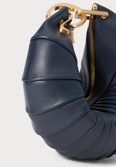 Navy leather handbag with a twisted design, accented by a gold zipper and hardware. The texture is smooth with quilted detailing.