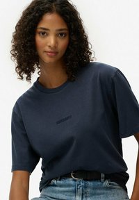 Granatowa bawełniana koszulka z krótkim rękawem i okrągłym dekoltem. Posiada subtelne haftowane logo "SUPERDRY" na piersi.