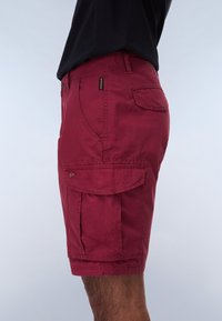 Pantaloni cargo rossi con tasca laterale, texture liscia e passanti per cintura. Il design prevede una vita standard e una vestibilità dritta.