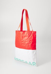 Sac fourre-tout rouge et blanc en matériau texturé, doté de deux anses orange et d'un imprimé turquoise sur la partie inférieure.