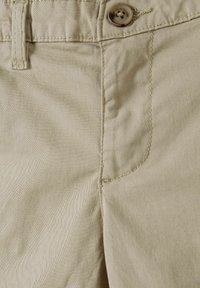 Beige bomullbyxor med en mjuk yta, som har en synlig knapp och överstygn, designade med en sid ficka fram.