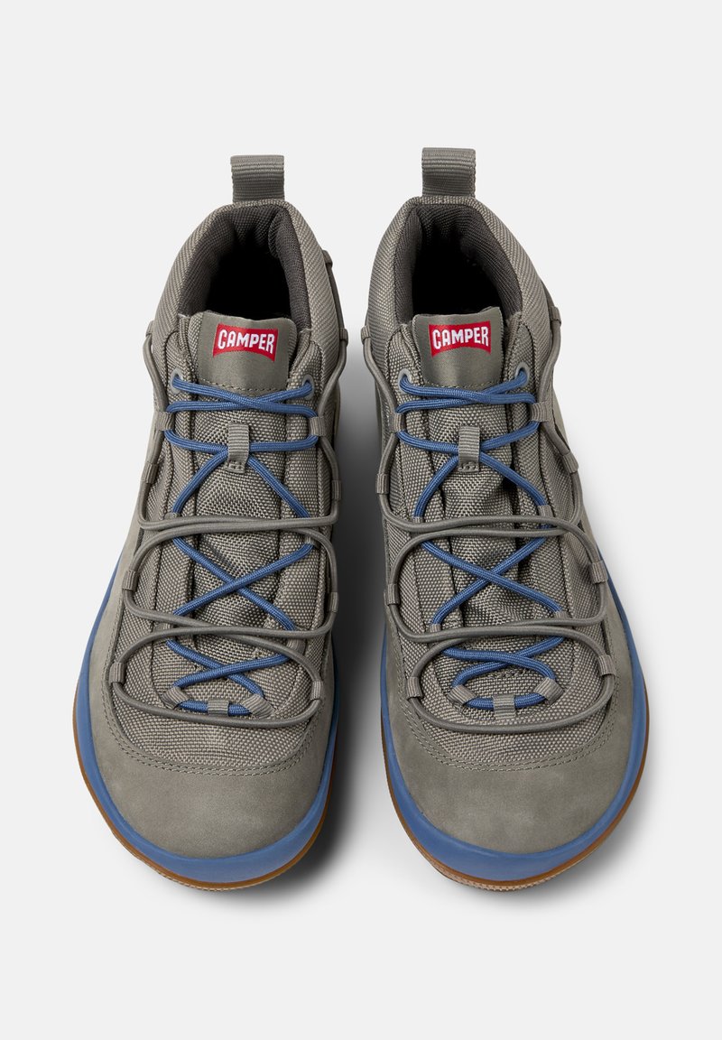 Grijze sportschoenen met blauwe veters en rubberen zolen, met bovenaan een opvallend rood "Camper" logo en een gestructureerd bovenwerk.
