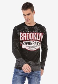 Schwarzes Langarmshirt mit Marmor-Muster, auffälligem "BROOKLYN"- und Markenlogo in Rot und Weiß, runder Ausschnitt und figurnahe Passform.