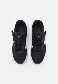 Baskets de sport noires avec tige en maille, logo Nike blanc et sangle réglable. Semelle texturée et intérieur rembourré pour le confort.