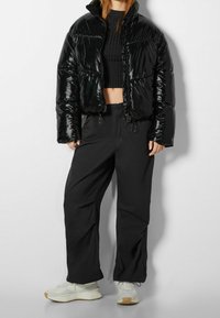 Černá lesklá prošívaná bunda s krátkým střihem, doplněná volnými černými kalhotami a bílými teniskami. Má vysoký límec a šňůrky na stažení.