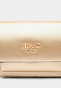 Kuldne nahast käekott, millel on sile tekstuur, esitleb reljeefset logo "LIU·JO MILANO" ning omab lihtsat ja puhast disaini.