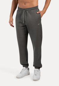 Grå sweatpants med elastisk talje, snor og smalle manchetter, parret med hvide sneakers. Minimalistisk design og komfortabel pasform.