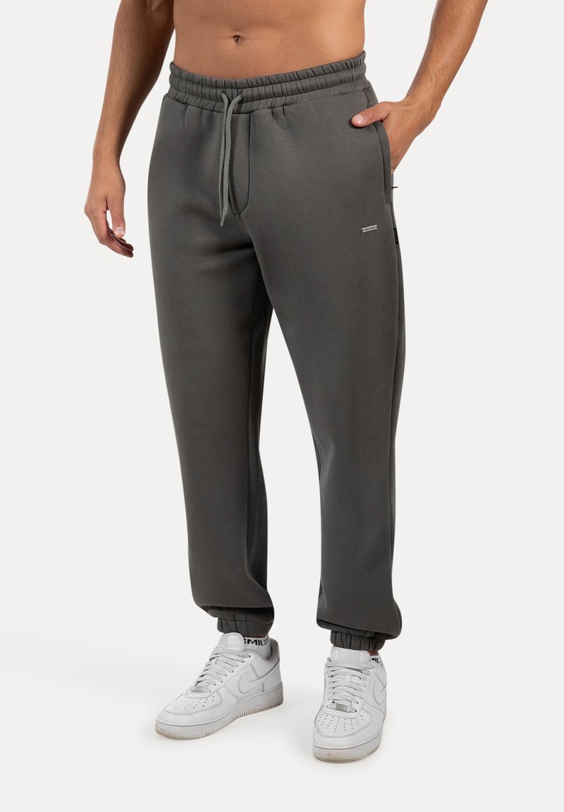 Grå sweatpants med elastisk talje, snor og smalle manchetter, parret med hvide sneakers. Minimalistisk design og komfortabel pasform.