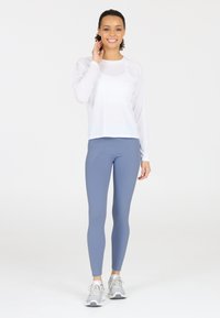 Vit långärmad träningströja med rundad nederkant, i kombination med ljusblå leggings med sid sömmar. Grå löparskor med snörning.
