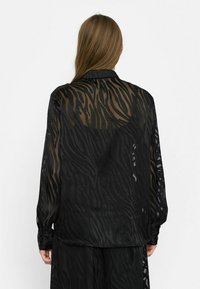 Sort gennemsigtig bluse med tigerstribe mønster, lange ærmer, krave og knapmanchetter, med en flydende, let struktur.