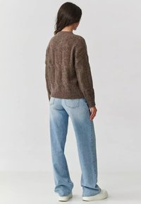 Brązowy sweter z dzianiny o fakturowanym wzorze, z okrągłym dekoltem i ściśniętymi mankietami, w połączeniu z jasnoniebieskimi spodniami z szerokimi nogawkami i białymi butami.