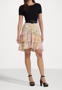 Černý žebrovaný top s krátkým rukávem v kombinaci s vrstvenou sukní s volánky a květinovým vzorem v pastelových barvách, staženou černým pásem. Černé boty na platformě.