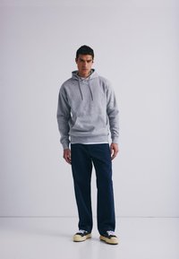 Grå hettegenser med frontlomme og snor, sammen med marineblå vide bukser og svarte joggesko med kremfarget såle. Enkel, uformell antrekk.