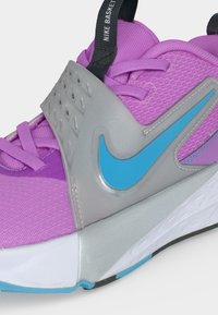Μωβ αθλητικό παπούτσι Nike με γκρι λουράκι, μπλε λογότυπο Swoosh, ροζ κορδόνια και λευκή σόλα με μπλε λεπτομέρειες στην εξωτερική σόλα.