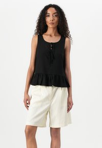 Čierny peplum top s okrúhlym výstrihom a viazaním v prednej časti, skombinovaný s krémovými krátkymi nohavicami s prúžkami, oboje z jemných látok.