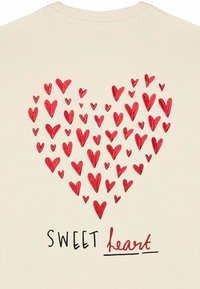 Felpa beige chiaro con una grafica composta da numerosi cuori rossi che formano una sagoma a cuore, con il testo "SWEET heart" in nero e rosso.