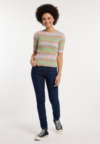 Top de punto de manga corta en verde pastel con rayas horizontales en rosa, azul y naranja; combinado con jeans ajustados azul oscuro y zapatillas negras.